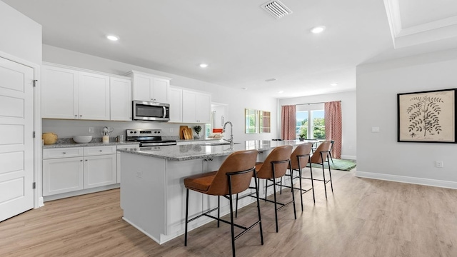 kitchen featuring white cabinetry, an island with sink, appliances with stainless steel finishes, and a kitchen bar