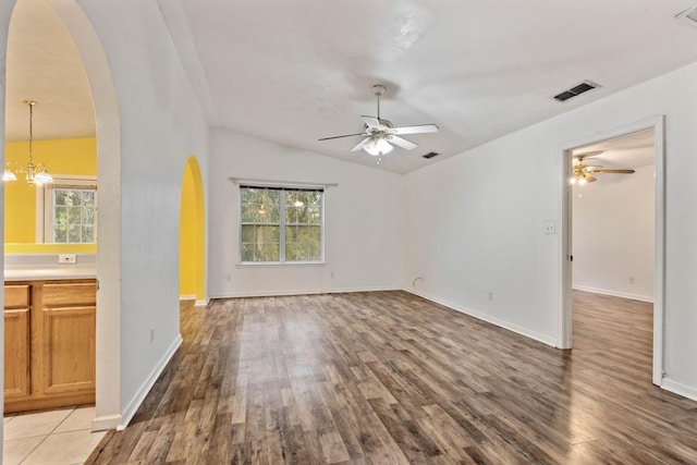 unfurnished living room featuring plenty of natural light, ceiling fan with notable chandelier, wood-type flooring, and vaulted ceiling