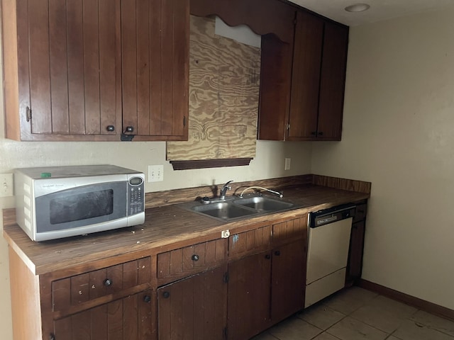 kitchen with dishwasher, light tile patterned flooring, dark brown cabinetry, and sink