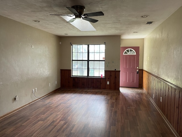 interior space with wood walls, dark hardwood / wood-style floors, ceiling fan, and a skylight