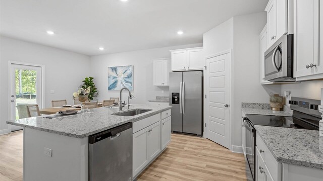 kitchen with stainless steel appliances, white cabinetry, sink, an island with sink, and light hardwood / wood-style flooring