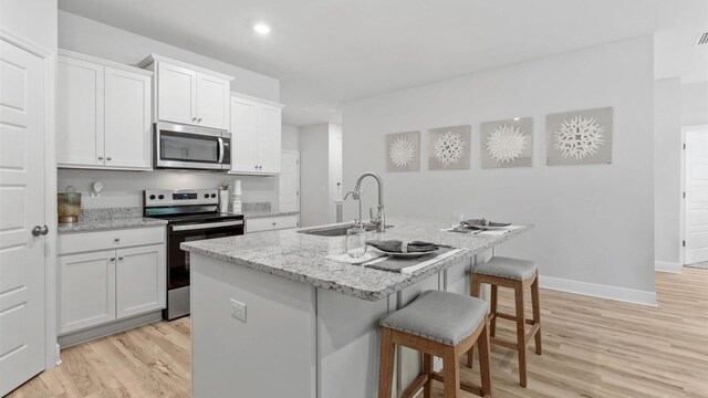 kitchen featuring a center island with sink, white cabinetry, appliances with stainless steel finishes, sink, and light hardwood / wood-style floors