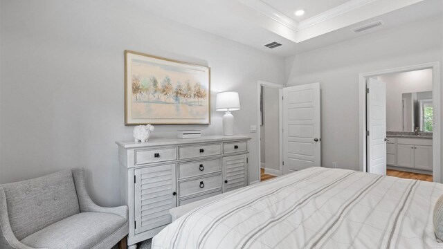 bedroom with ornamental molding, light wood-type flooring, ensuite bath, and a tray ceiling