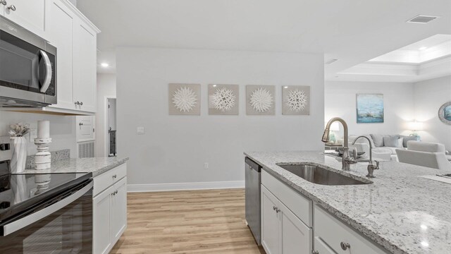 kitchen featuring stainless steel appliances, white cabinetry, sink, light stone counters, and light wood-type flooring