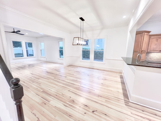 unfurnished dining area featuring crown molding, ceiling fan with notable chandelier, and light hardwood / wood-style floors