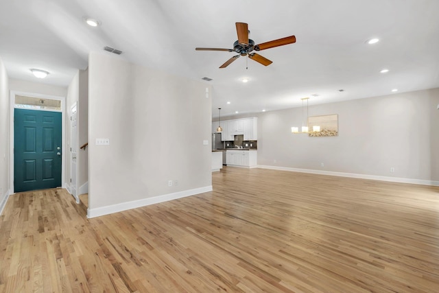 unfurnished living room featuring ceiling fan with notable chandelier and light hardwood / wood-style flooring