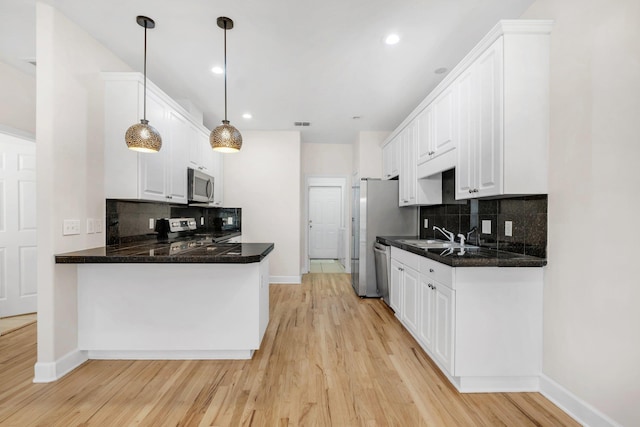 kitchen with appliances with stainless steel finishes, tasteful backsplash, pendant lighting, white cabinets, and light hardwood / wood-style floors