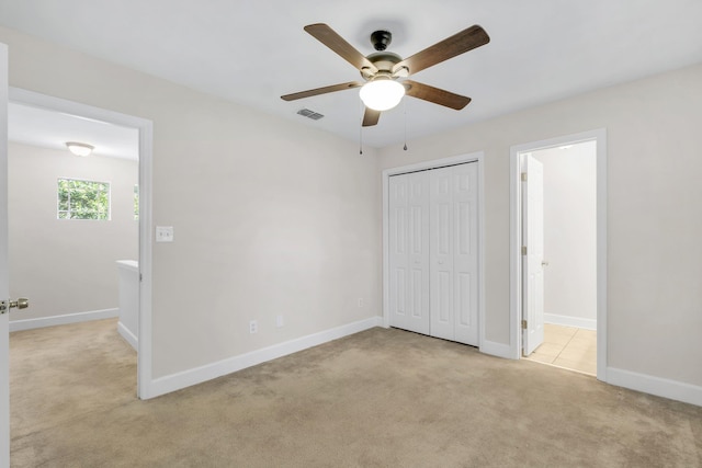 unfurnished bedroom with ensuite bath, ceiling fan, a closet, and light colored carpet