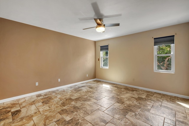 unfurnished room featuring stone finish flooring, ceiling fan, and baseboards