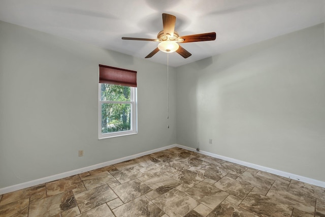 unfurnished room featuring stone finish floor, baseboards, and a ceiling fan