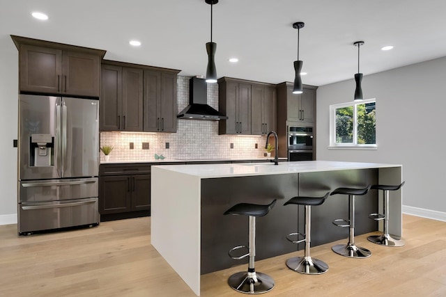 kitchen with wall chimney exhaust hood, light hardwood / wood-style flooring, decorative light fixtures, stainless steel appliances, and sink