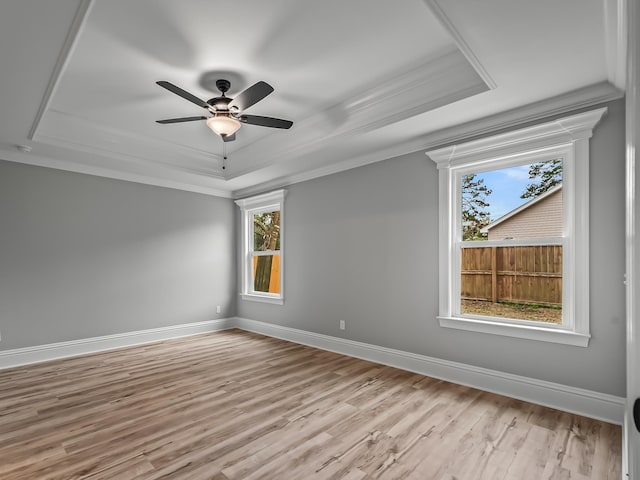 empty room with crown molding, ceiling fan, a tray ceiling, and light wood-type flooring