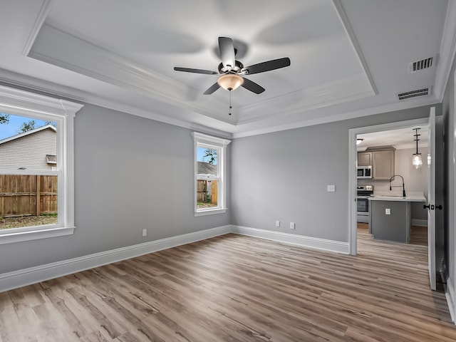 interior space with wood-type flooring, ceiling fan, crown molding, and a tray ceiling