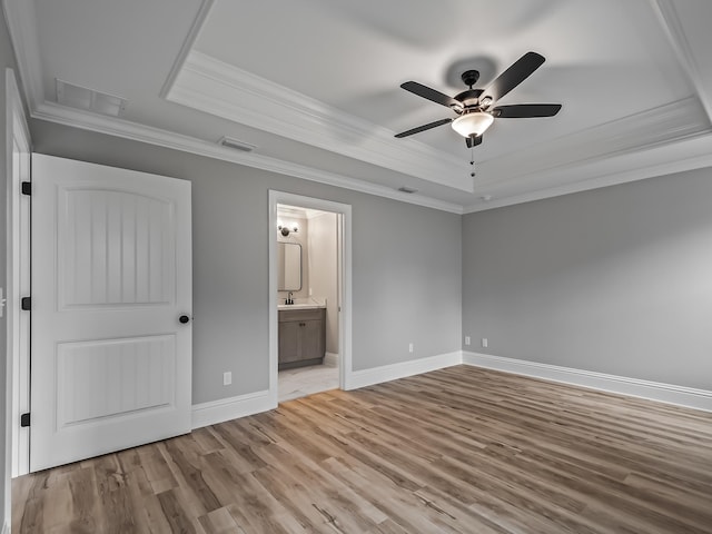 unfurnished bedroom featuring a tray ceiling, ornamental molding, light hardwood / wood-style floors, and ensuite bath