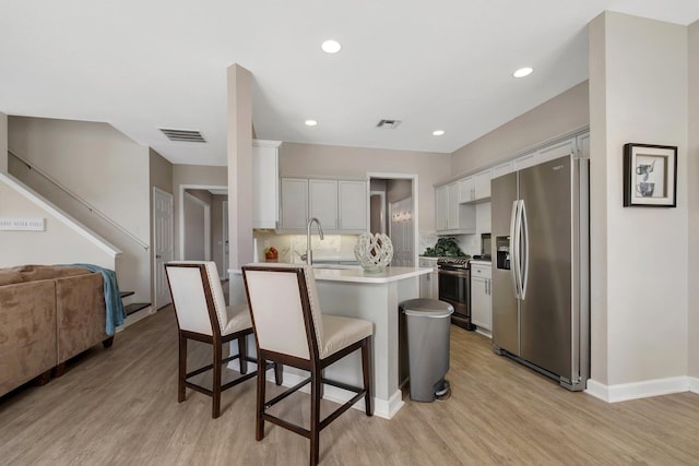 kitchen featuring appliances with stainless steel finishes, a breakfast bar, sink, white cabinets, and light wood-type flooring