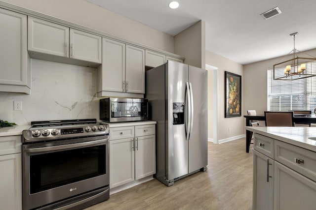 kitchen featuring appliances with stainless steel finishes, gray cabinetry, an inviting chandelier, and decorative backsplash