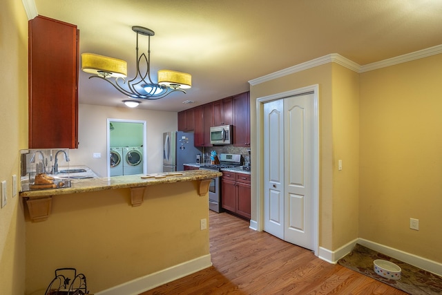 kitchen with kitchen peninsula, appliances with stainless steel finishes, washer and clothes dryer, decorative light fixtures, and light hardwood / wood-style flooring