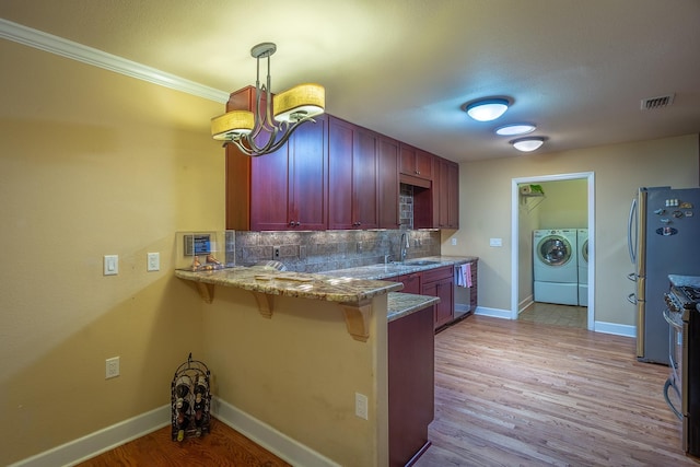 kitchen featuring sink, tasteful backsplash, decorative light fixtures, kitchen peninsula, and washing machine and clothes dryer