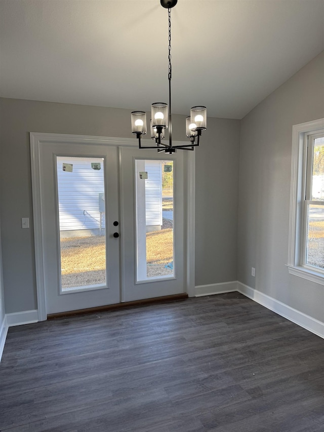 unfurnished dining area featuring lofted ceiling, dark hardwood / wood-style flooring, a wealth of natural light, and an inviting chandelier