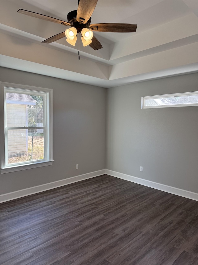 empty room with a tray ceiling, dark hardwood / wood-style floors, and ceiling fan