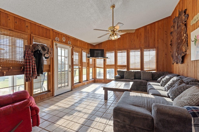 tiled living room with vaulted ceiling, ceiling fan, wood walls, and a textured ceiling