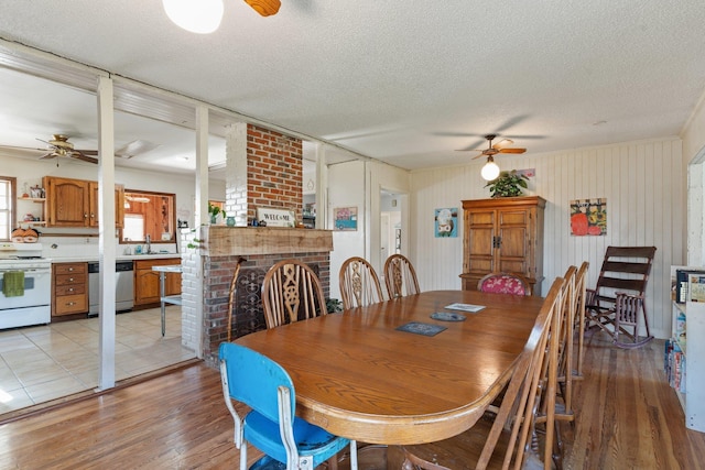 dining area featuring light wood-style floors, a fireplace, ceiling fan, and a textured ceiling