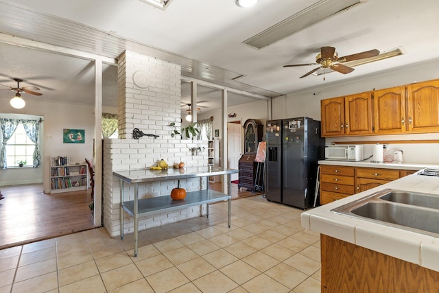 kitchen featuring light tile patterned floors, white microwave, ceiling fan, brown cabinets, and black fridge