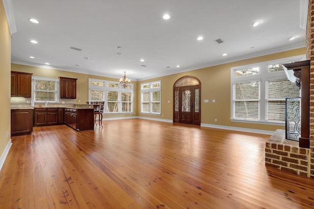 unfurnished living room with crown molding, a notable chandelier, and light wood-type flooring