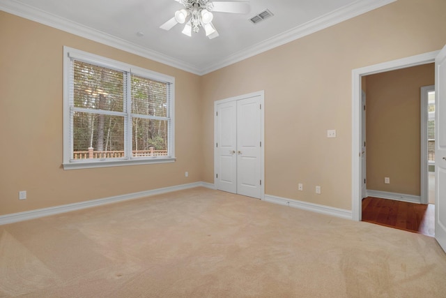 unfurnished bedroom featuring ornamental molding, light colored carpet, ceiling fan, and a closet