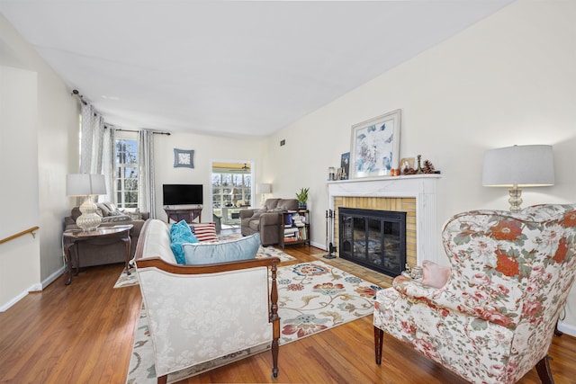 living area with a brick fireplace, baseboards, and wood finished floors