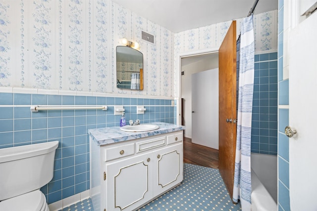 full bathroom featuring a wainscoted wall, tile walls, visible vents, toilet, and wallpapered walls