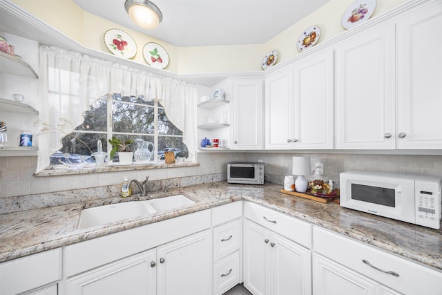 kitchen featuring open shelves, white microwave, a sink, and white cabinetry