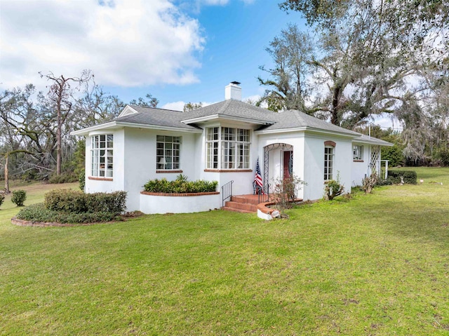 view of front of house with stucco siding, a shingled roof, a chimney, and a front yard