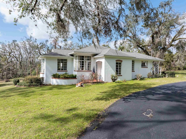 single story home featuring a front lawn, a shingled roof, and stucco siding