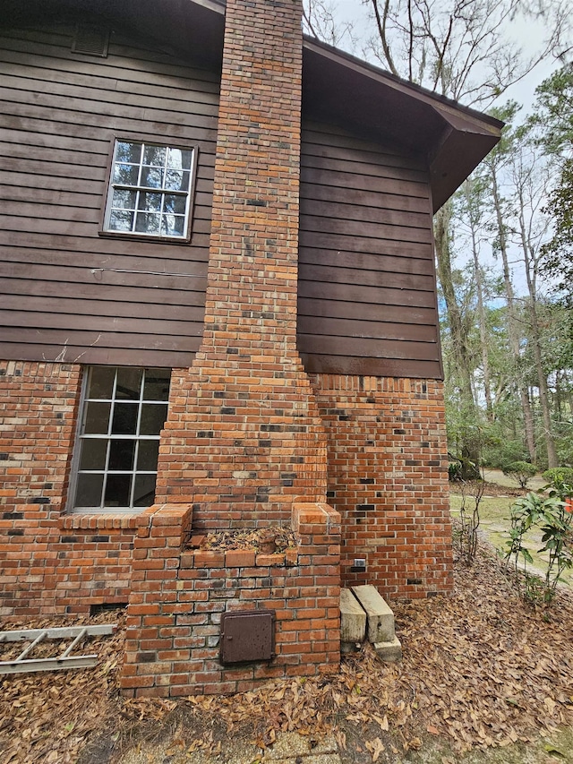 view of side of home with brick siding, crawl space, and a chimney