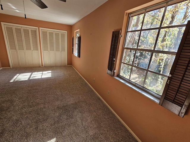 unfurnished bedroom featuring carpet floors, baseboards, and two closets