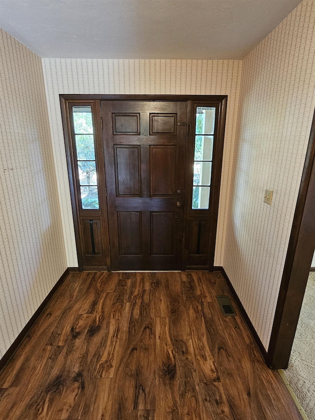 interior space featuring wallpapered walls, baseboards, visible vents, and dark wood finished floors