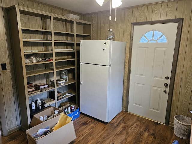 kitchen featuring dark wood-type flooring, freestanding refrigerator, crown molding, and wooden walls