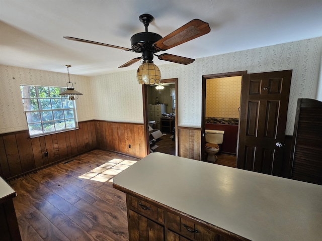 interior space featuring dark wood-type flooring, wainscoting, a ceiling fan, and wallpapered walls