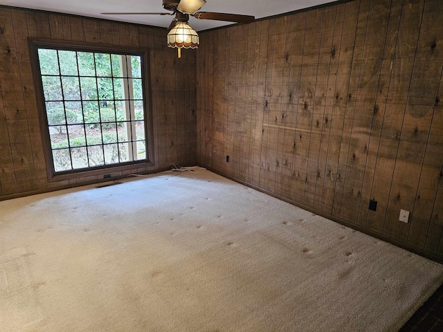 carpeted empty room featuring a ceiling fan and wooden walls