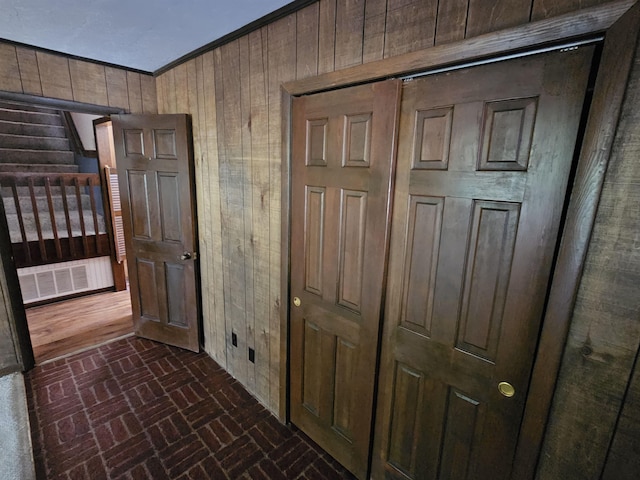 corridor featuring brick floor, visible vents, wood walls, and crown molding