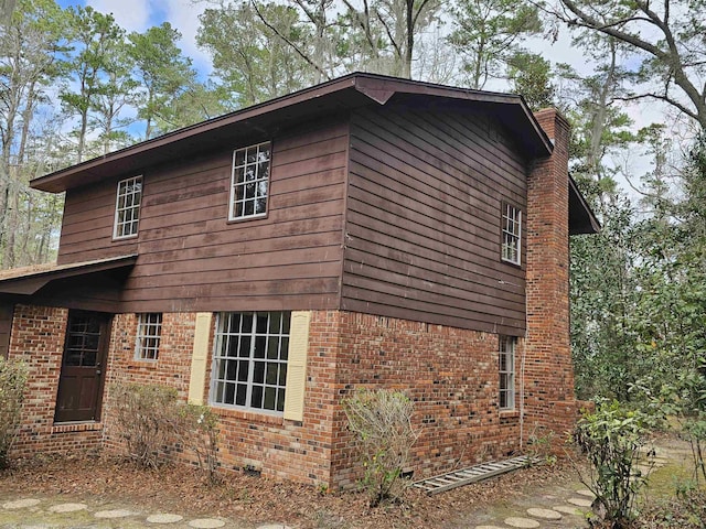 view of home's exterior with crawl space, a chimney, and brick siding