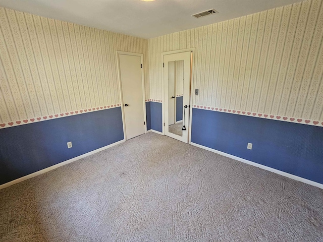 carpeted spare room featuring visible vents, baseboards, and wallpapered walls