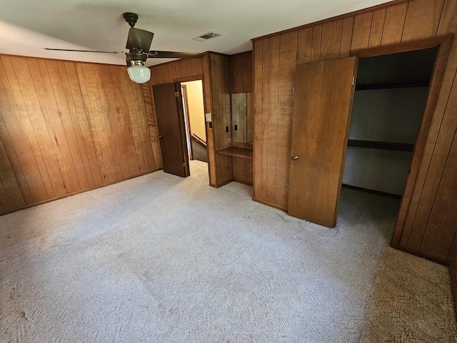 unfurnished bedroom featuring wooden walls, light carpet, visible vents, a spacious closet, and a closet