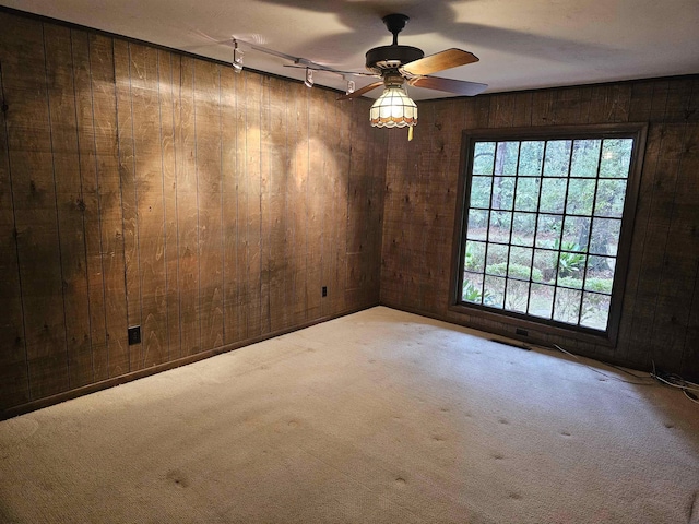 empty room featuring ceiling fan, wooden walls, rail lighting, and light colored carpet