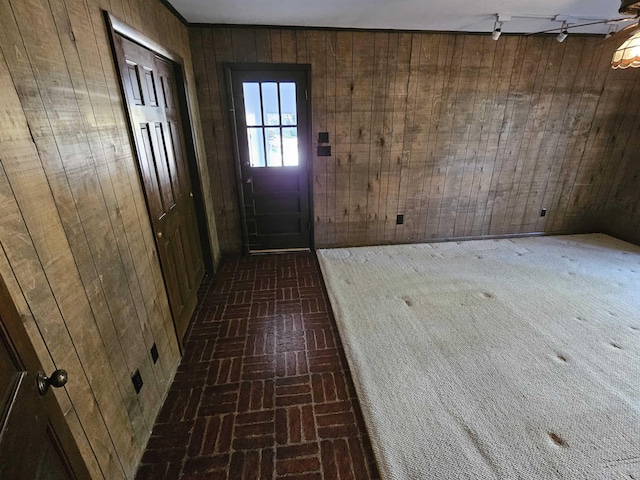 entryway with brick floor, wooden walls, and rail lighting