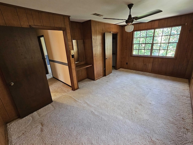 unfurnished bedroom with light carpet, wood walls, ceiling fan, and visible vents