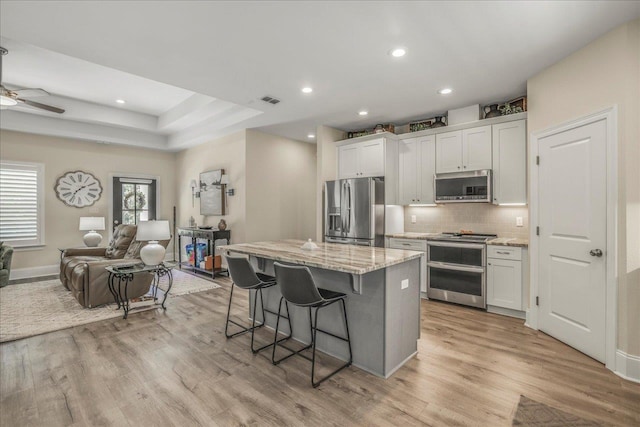 kitchen featuring open floor plan, a center island, stainless steel appliances, a breakfast bar area, and light wood finished floors