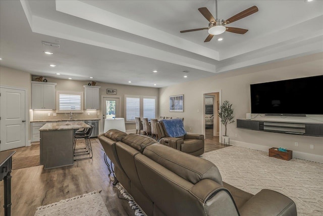 living area featuring wood finished floors, baseboards, recessed lighting, ceiling fan, and a raised ceiling