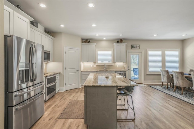 kitchen featuring a breakfast bar area, a kitchen island, a sink, decorative backsplash, and appliances with stainless steel finishes